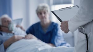 doctor with chart talking to sick patient and spouse in a hospital room