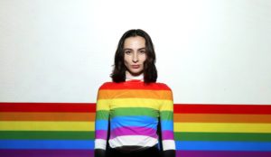 person with rainbow shirt standing against rainbow background